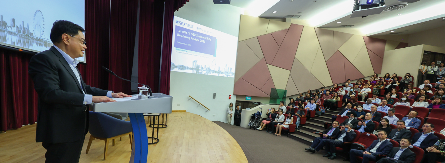 SGXFIRST event: Man at podium in suit addresses seated audience; screen shows logo and Singapore skyline.